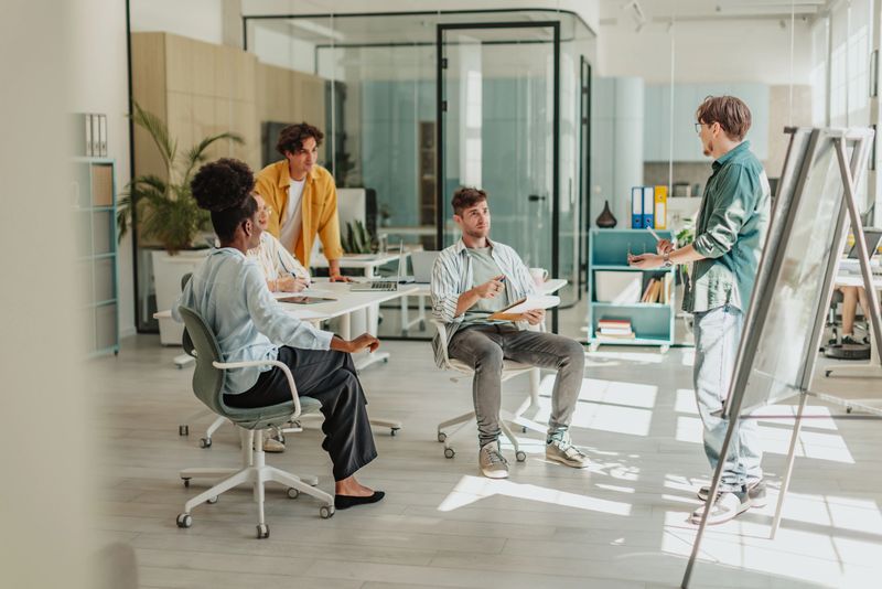 A diverse group of young adults engages in a collaborative meeting in a contemporary office environment. They share ideas and communicate effectively while enjoying the work process.