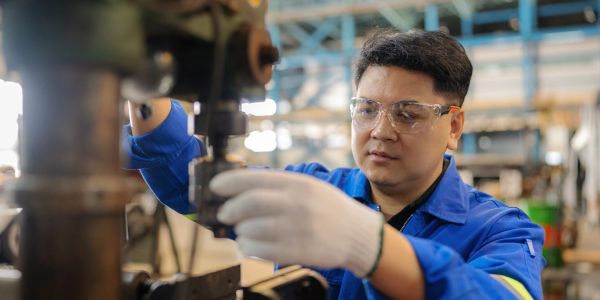 Worker operating industrial machinery wearing safety glasses.