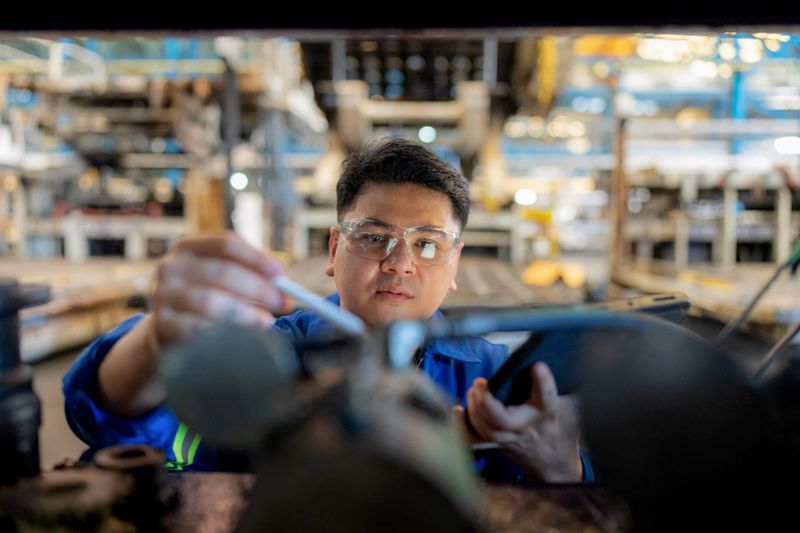Maintenance engineer in protective workwear examines vehicle parts using digital technology for precision and quality control. Concept of manufacturing, safety, inventory management, and teamwork in the automobile industry.