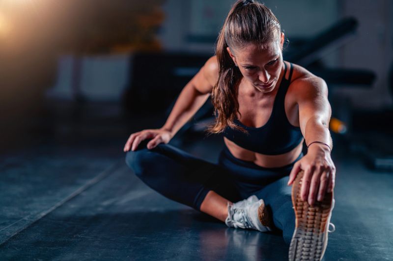Stretching after a gym workout, a woman improves mobility and eases muscle stiffness. This practice enhances recovery and fosters long-term health with targeted post exercise care.