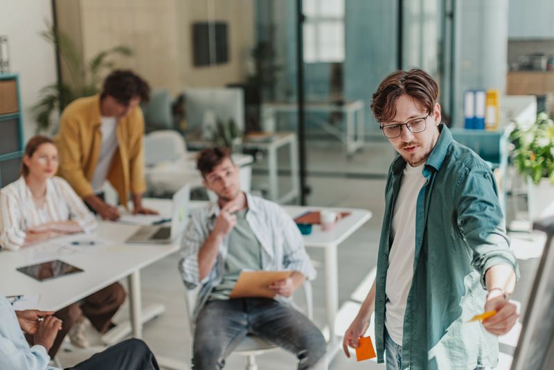 A group of young adults collaborates in a bright, modern office setting. They discuss ideas and share notes, demonstrating teamwork and open communication.