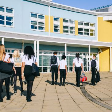 Students walking towards a modern school building on a sunny day.