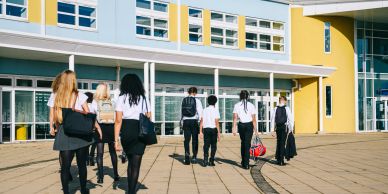 Students walking towards a modern school building on a sunny day.