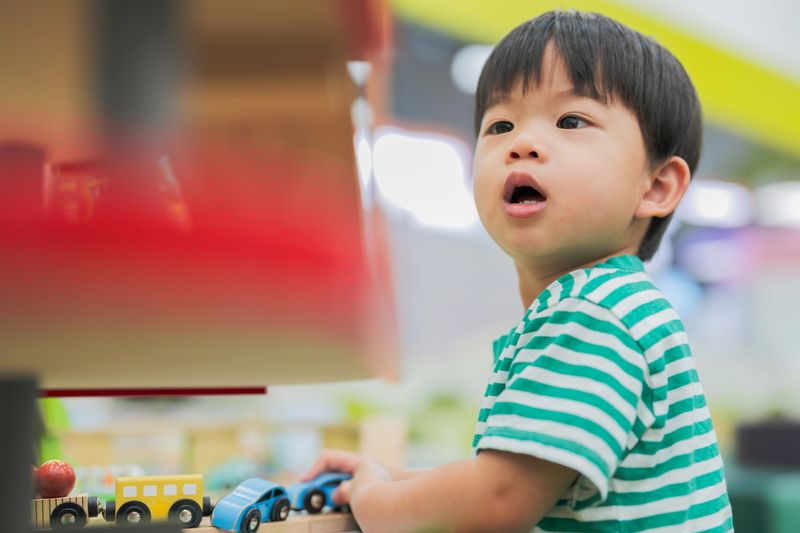Cheerful Asian boy develops cognitive skills and muscle coordination through playful exploration with colorful plastic toys at indoor playground, fostering brain development and creative problem solving abilities