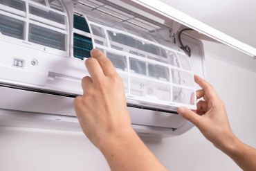 Hands removing a filter from an air conditioner unit.