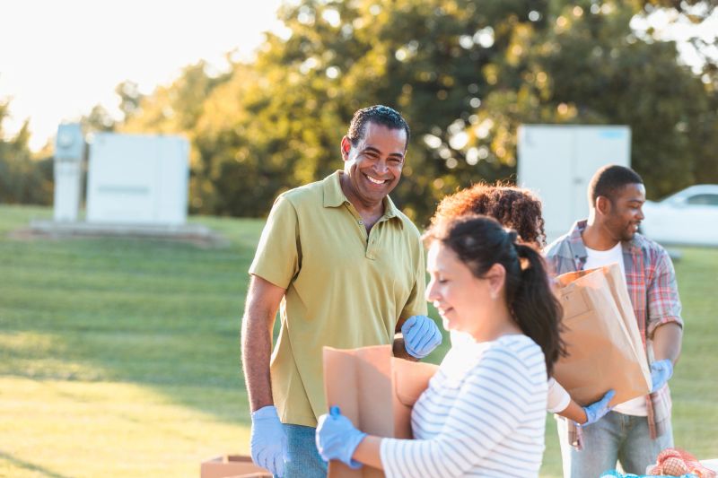 Volunteers of diverse ethnicities and ages collaborate outdoors, holding paper bags, participating in a community outreach initiative or donation event.