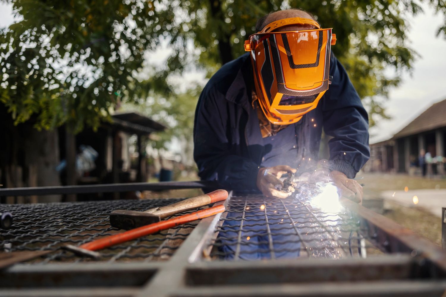 Person welding metal outdoors wearing an orange protective mask.