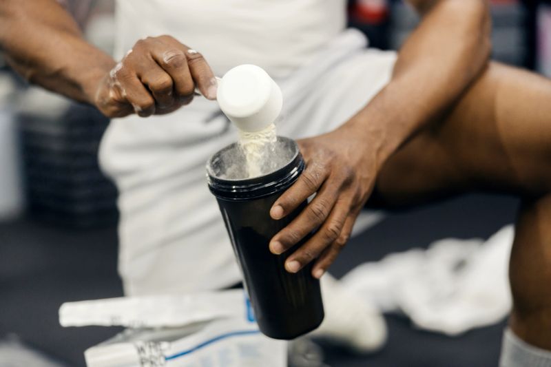 Man scooping protein powder into a shaker bottle, preparing a post-workout drink for muscle building and fitness