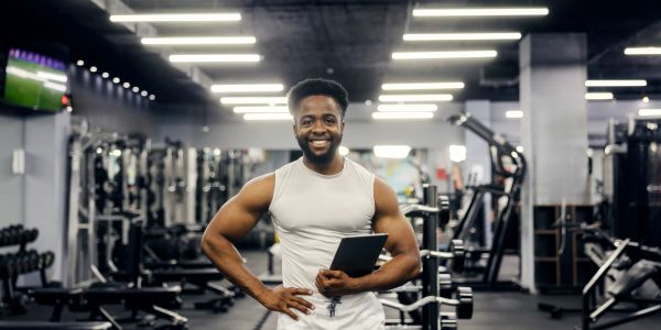 A smiling man holding a tablet in a gym.
