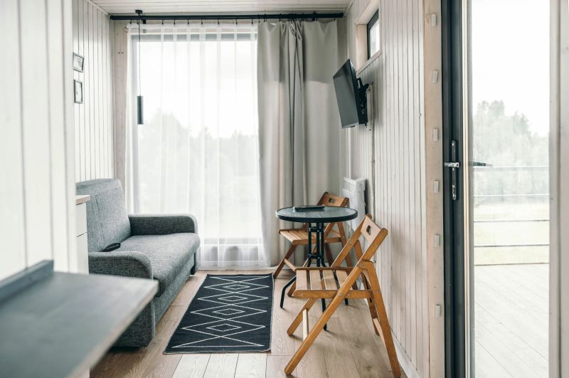 Cozy interior of a vacation rental with a gray sofa, wooden table, and chairs. Large windows allow natural light, creating a relaxing atmosphere for an escape.