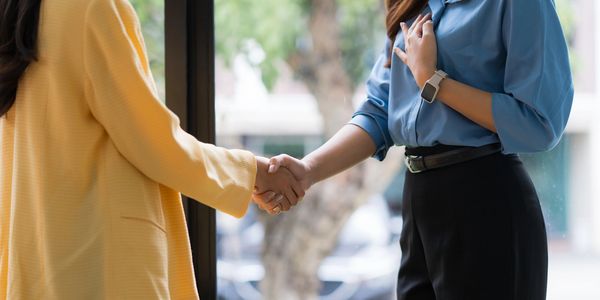 Two women shaking hands in a professional setting by a window.