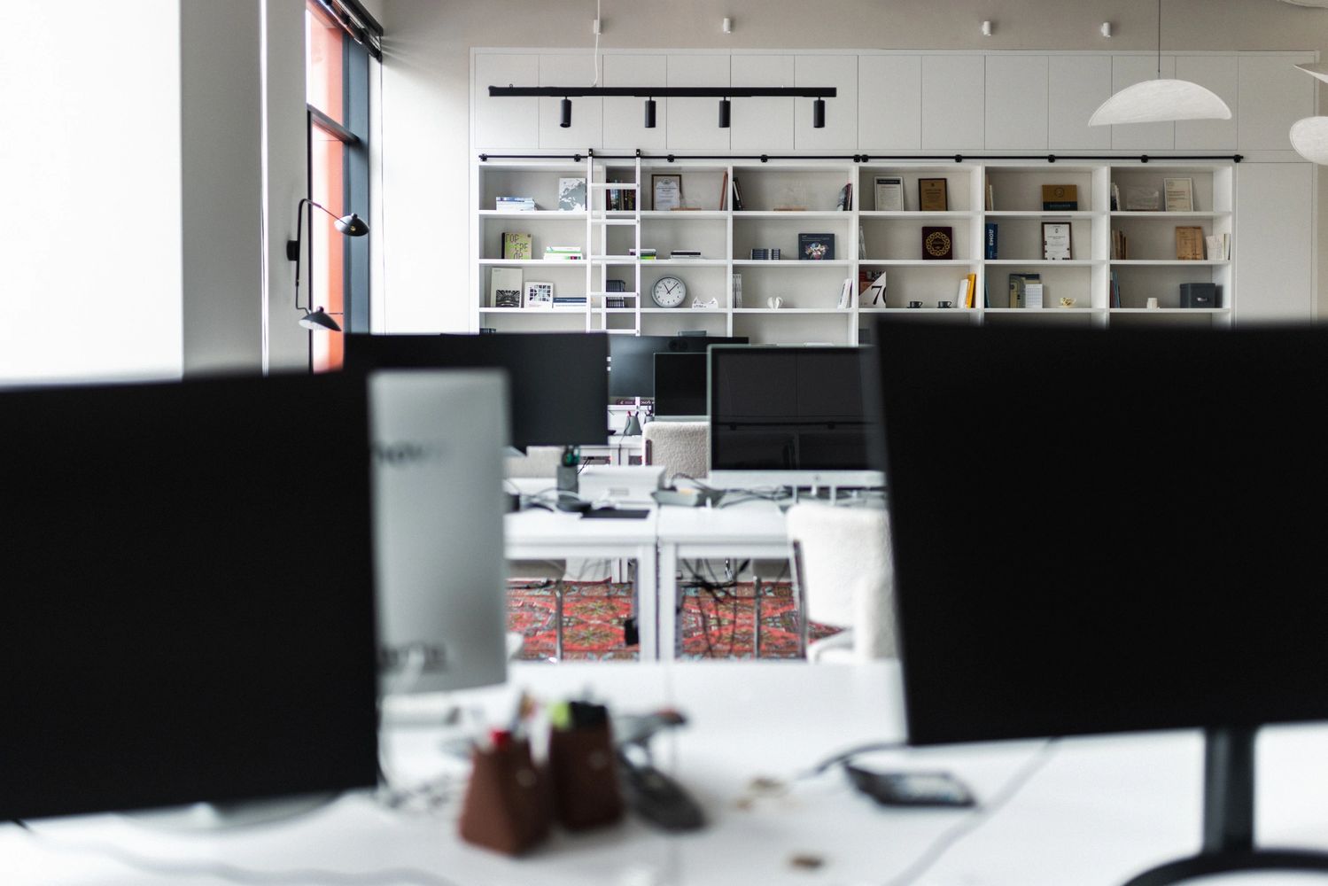Modern office with multiple computer monitors and a large bookshelf.