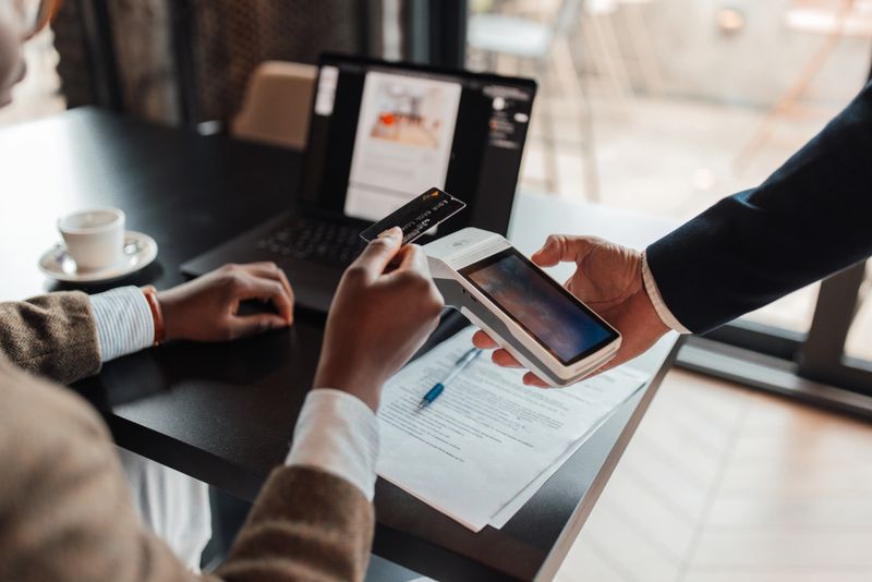 A customer processing a payment with a credit card by a mobile device while sitting at a cafe table, enhancing the perception of modern payment solutions.