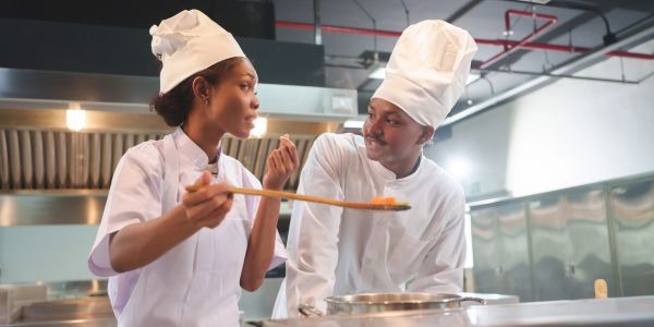 Two chefs tasting food in a modern kitchen.