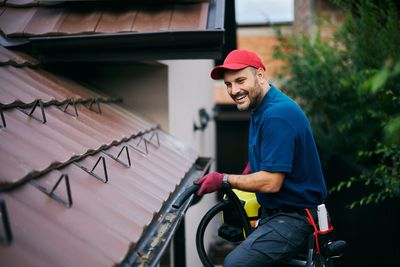 A man cleaning gutters on a house roof with equipment.