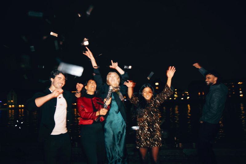 A group of friends having fun celebrating during the night accompanied by confetti and joyful expressions, showcasing camaraderie and a festive atmosphere.