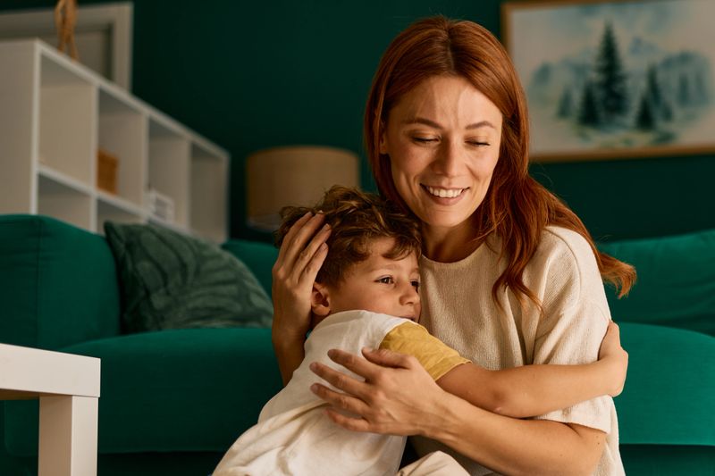 Happy mother and young son share a warm, tender hug in their cozy living room, smiling and enjoying a loving family moment of comfort, affection and togetherness