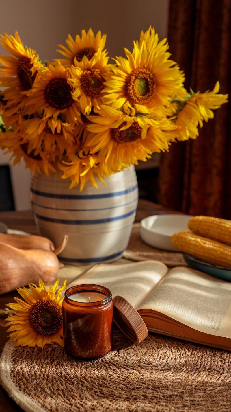 A warm and inviting still life features a bouquet of sunflowers, a lit candle, and an open book, creating a cozy atmosphere.