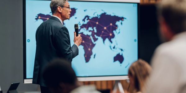 Businessman giving a presentation with a world map on screen.
