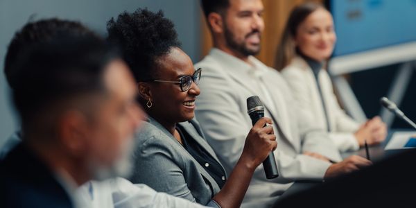 Woman speaking into a microphone at a panel discussion.