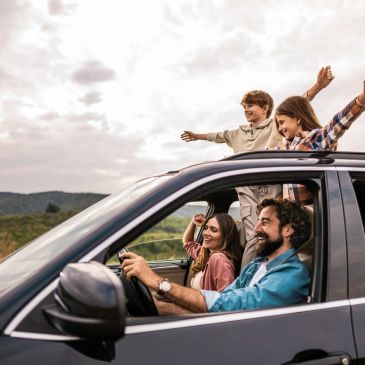 Happy family enjoying a car trip with kids standing through the sunroof.