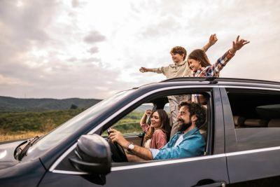 Family enjoying a road trip with kids standing through the sunroof.