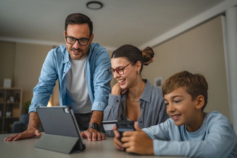 Parents and child shopping online at home, mother holding credit card while father and son view a digital tablet together, enjoying browsing and making a purchase on-screen