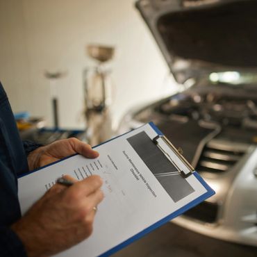 A mechanic holding a clipboard with a car inspection checklist near an open car hood.