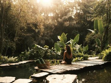 Woman sitting on a wooden bridge in a lush forest.