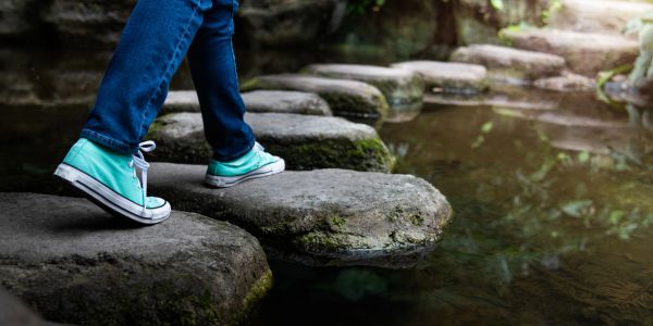 Person walking on stepping stones across water.