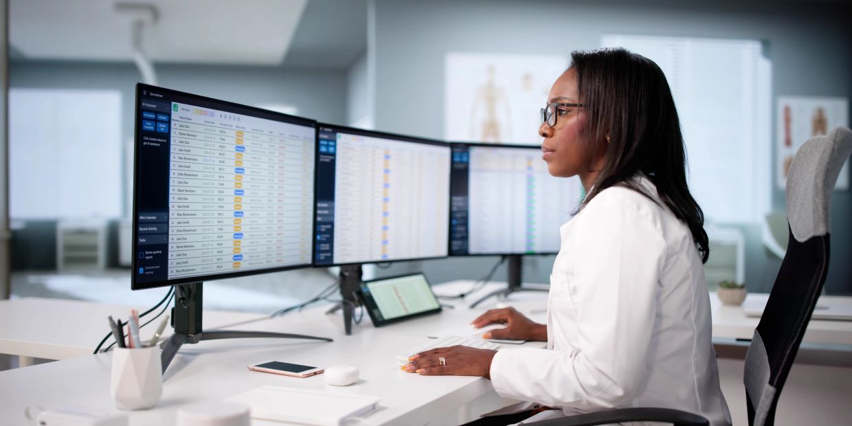 A professional woman analyzes data on multiple monitors in a modern office.