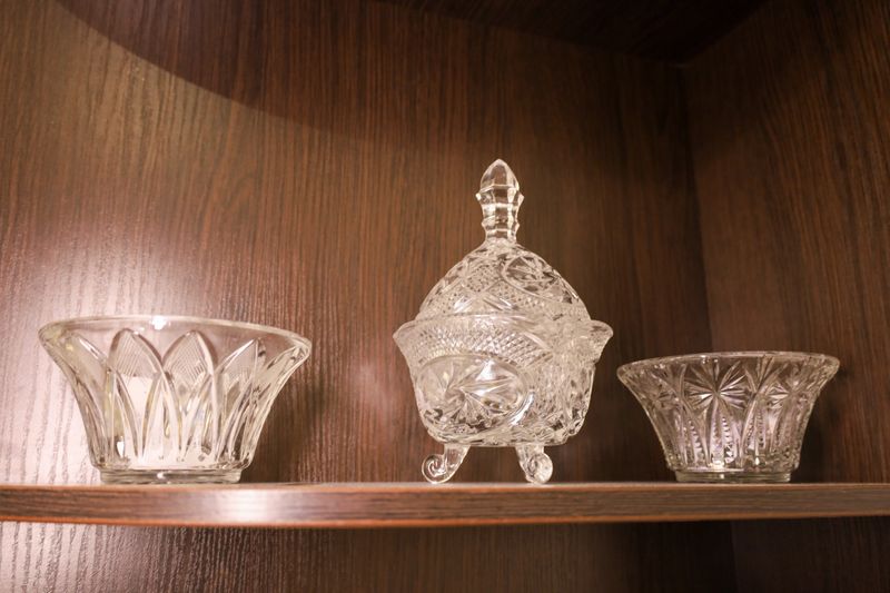 ​An elegant collection of crystal glassware, consisting of a central candy dish on legs and two side bowls, adorns a dark wooden shelf.