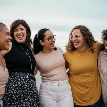 Group of five diverse women smiling and enjoying each other's company outdoors.