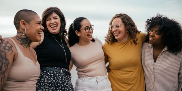 Five diverse women smiling and standing close together.
