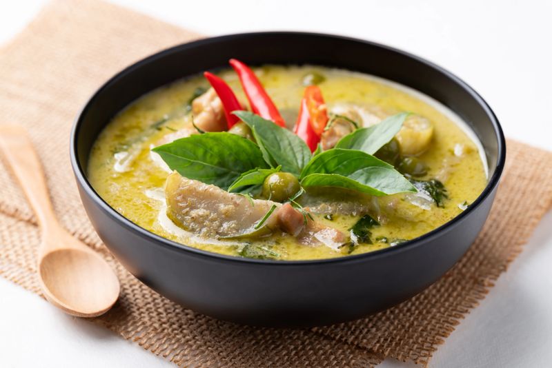 Thai green curry chicken in black bowl with spoon on white background
