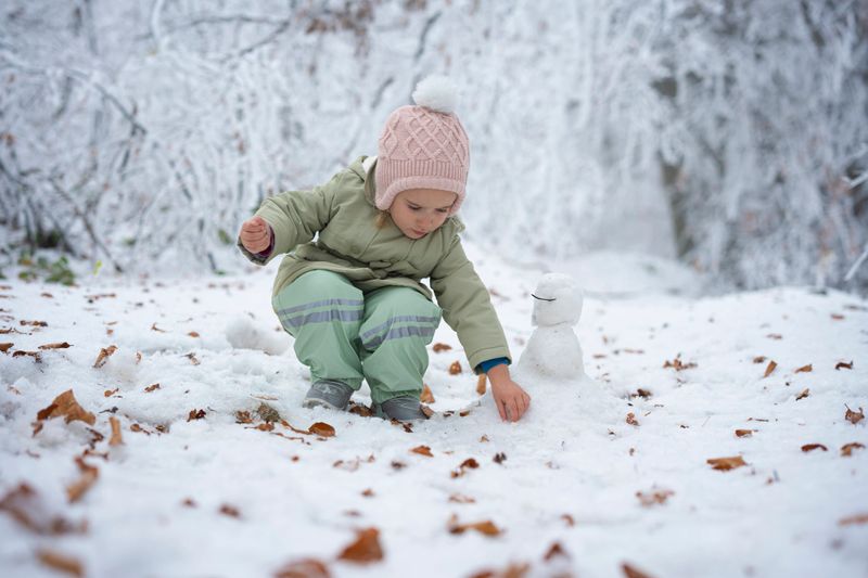 Happy childhood. Play time in winter, little concentrated girl doing a snowman in the forest after big snowfall.