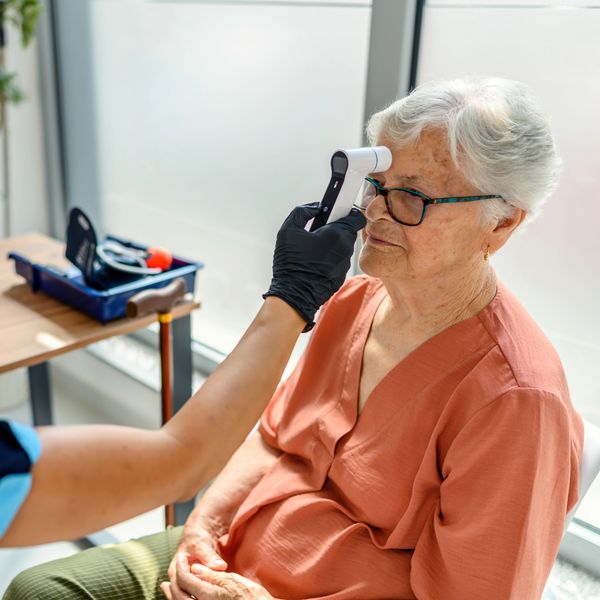 A healthcare worker checks an elderly woman's temperature with a forehead thermometer.
