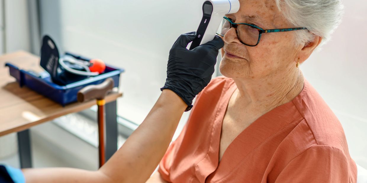Healthcare worker checks elderly woman's temperature with a forehead thermometer.