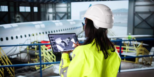 Engineer using a tablet to inspect airplane parts in a hangar.