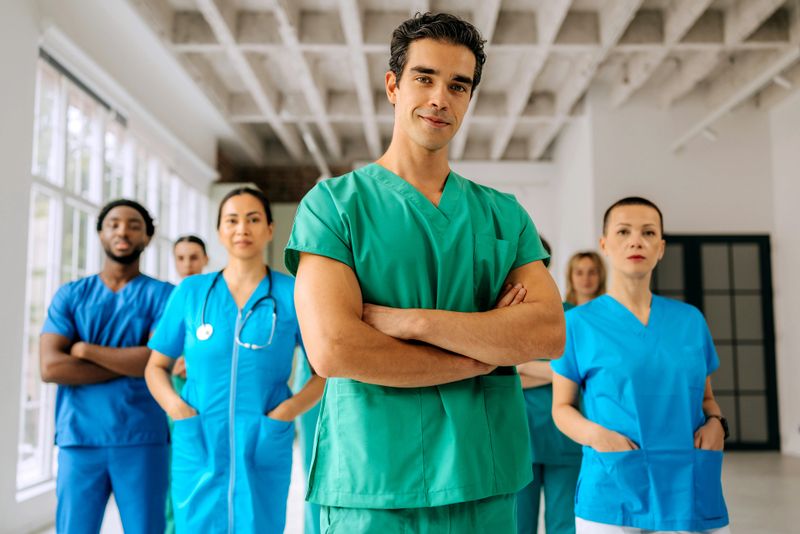 Team of healthcare professionals standing together and smiling at the camera, with a confident male doctor positioned in front. Represents teamwork, leadership, and unity in the medical field