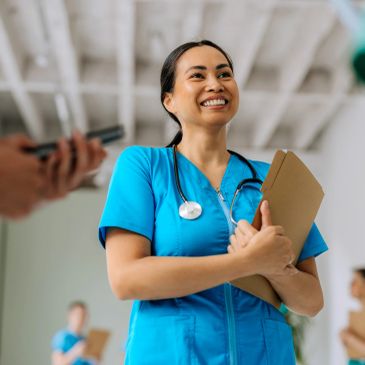 Smiling nurse in blue scrubs holding a clipboard.
