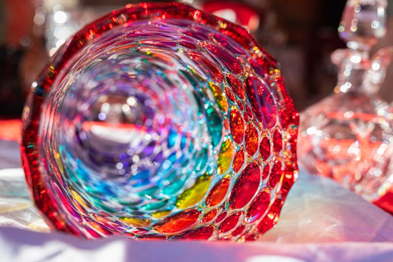 Vibrant glass vase lying on an antique market stall, illuminated by soft morning light, capturing intricate details and reflections