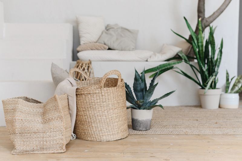 Beautiful handcrafted jute baskets standing on a soft rug near lush green plants. Natural home decoration in boho and eco style. Warm light, neutral colors and textures create a calm and cozy interior mood.