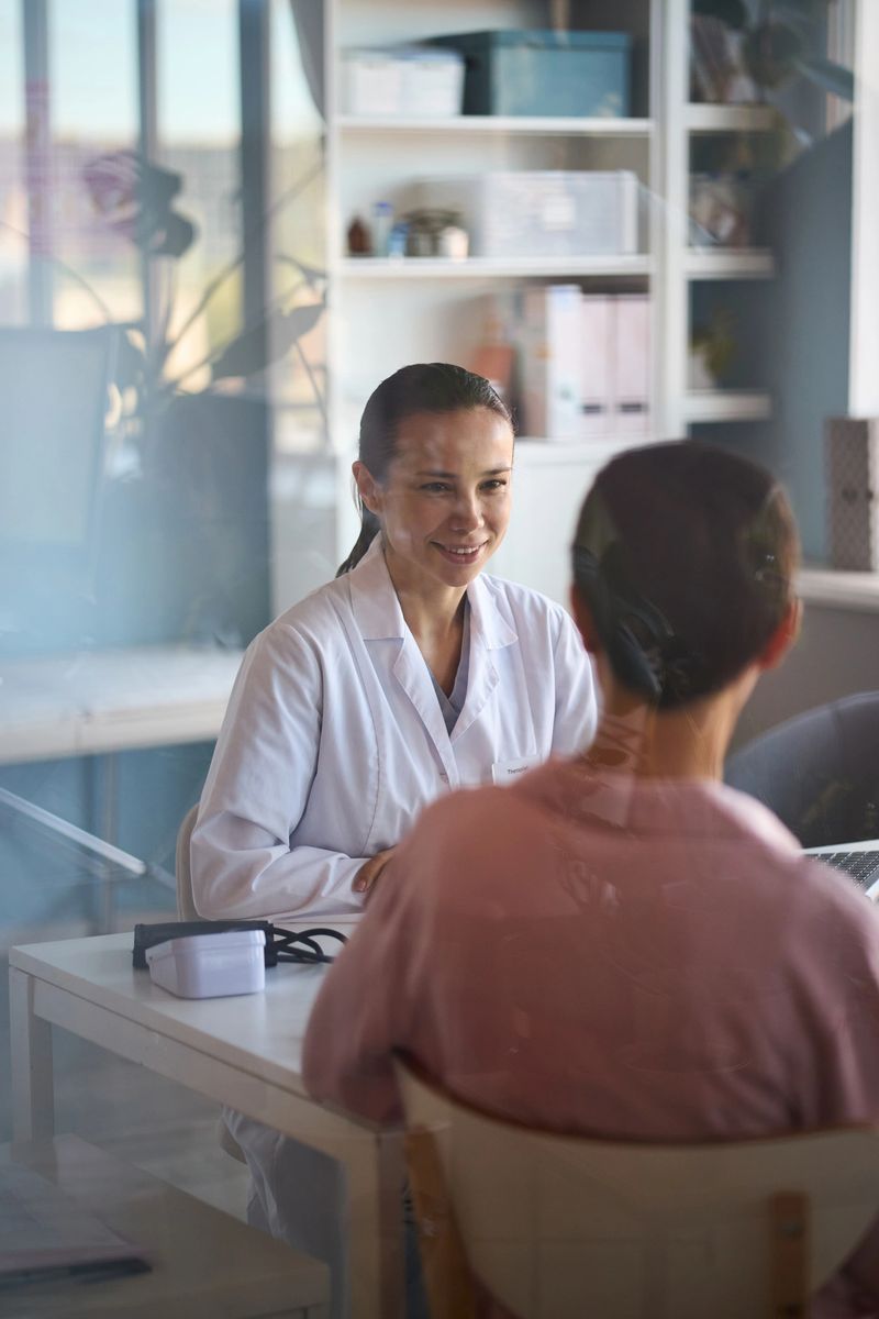 Caucasian female doctor smiling while consulting middle aged Caucasian woman with short hair in medical office, discussing cancer diagnosis or treatment options during appointment
