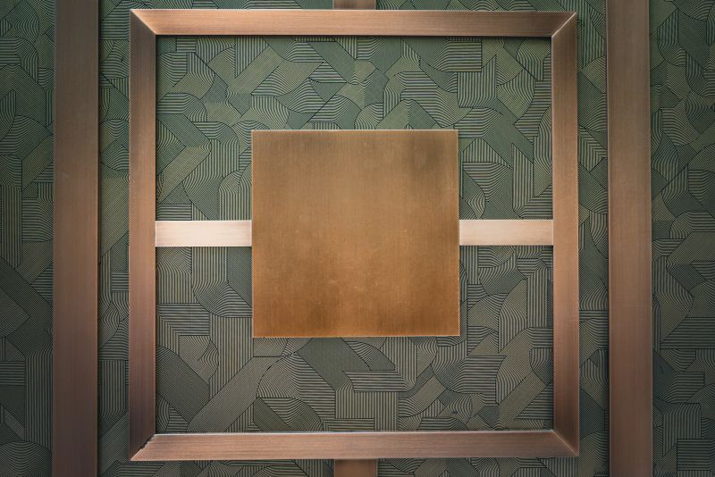 A contemporary abstract composition featuring geometric bronze shapes mounted against a patterned wall. The image blends modern design, symmetry, and texture, highlighting the elegance of metallic tones and architectural form.