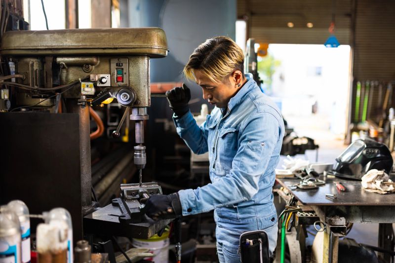 A professional metal worker is operating a drilling machine in a metal workshop.