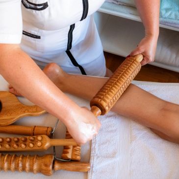 Therapist massaging leg with wooden roller tools.
