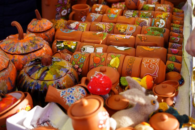 Brightly colored pottery and crafts are arranged at a market. People admire the intricate designs on pots and figurines during a sunny afternoon.