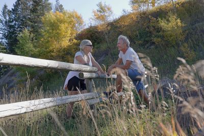 An elderly couple chatting outdoors by a wooden fence in nature.
