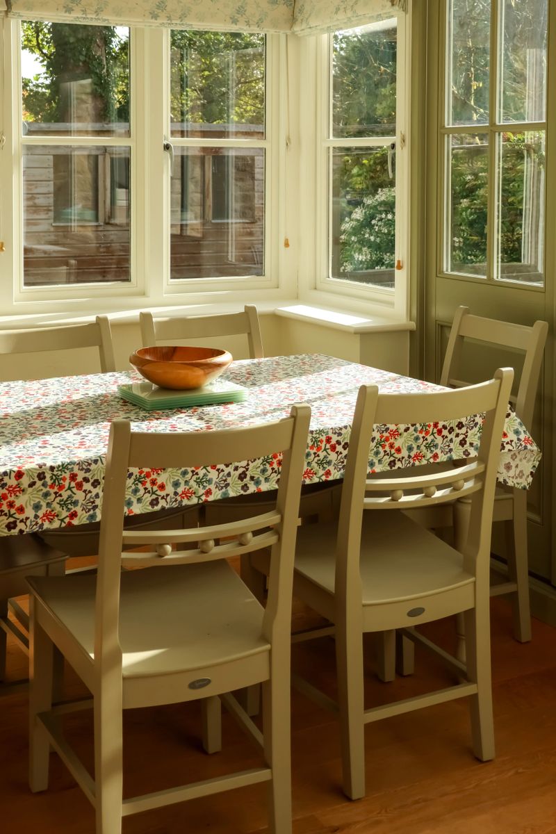 Cozy dining room bay window with floral tablecloth and chairs, enjoying natural light. Cotswolds countryside, England